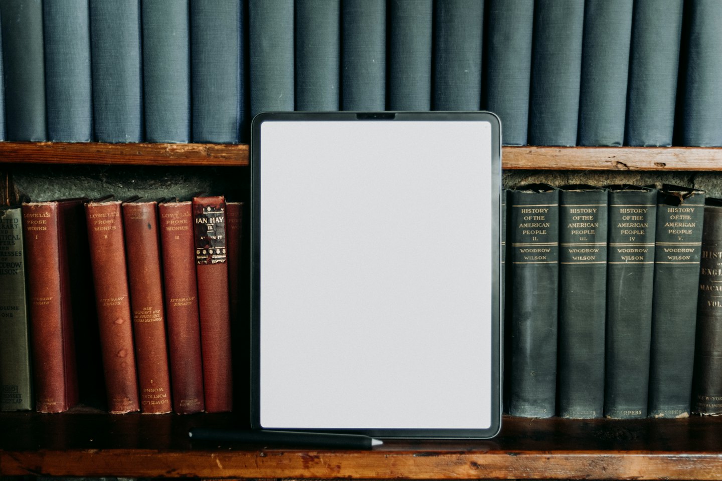 Tablet and antique books on a wooden shelf.