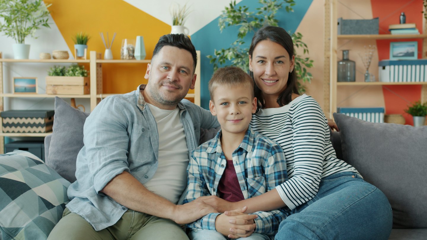 Family smiling on a grey sofa in a modern living room.